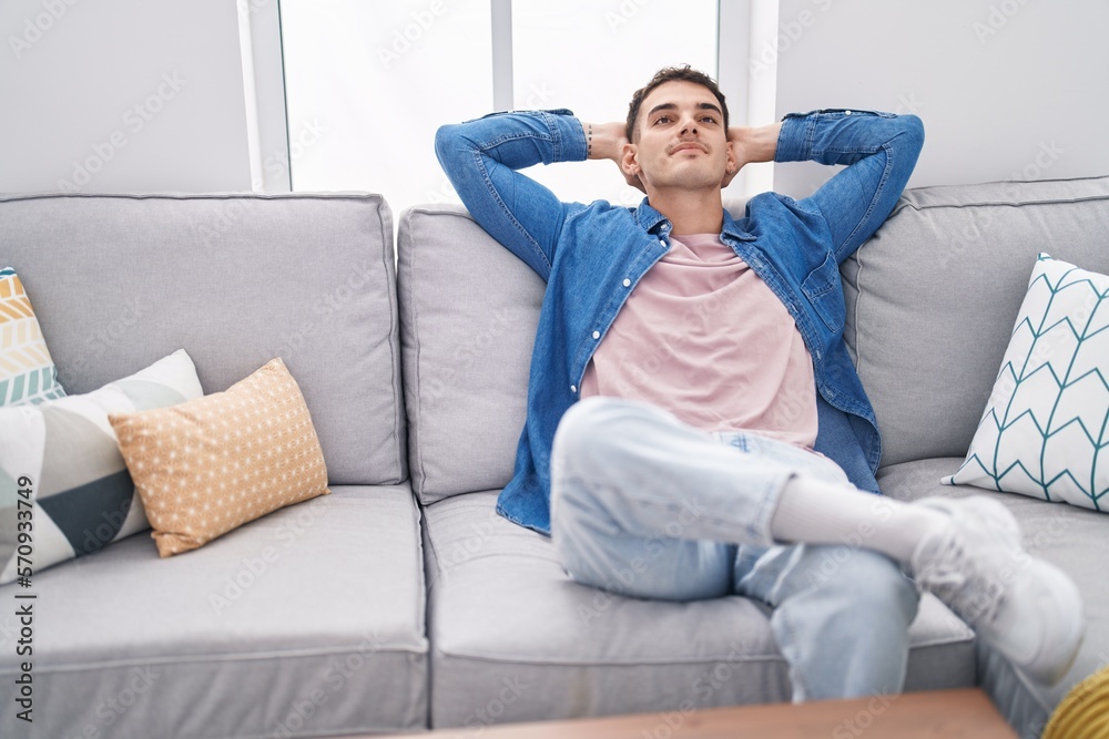 Young hispanic man relaxed with hands on head sitting on sofa at home