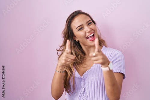 Young hispanic woman standing over pink background pointing fingers to camera with happy and funny face. good energy and vibes. © Krakenimages.com