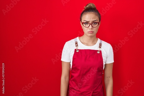 Young hispanic woman wearing waitress apron over red background skeptic and nervous, frowning upset because of problem. negative person. photo
