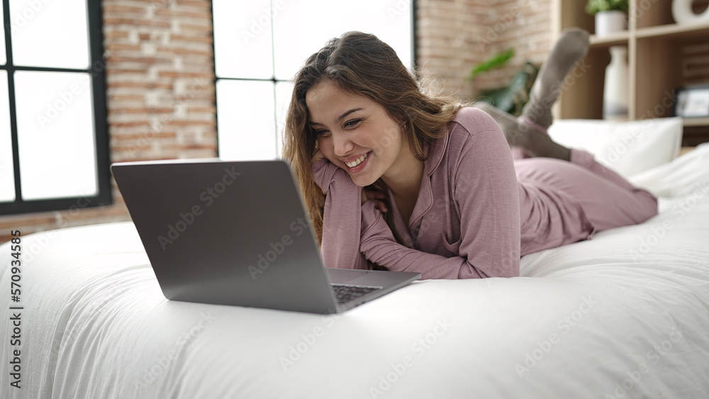 Naklejka premium Young beautiful hispanic woman using laptop lying on bed at bedroom