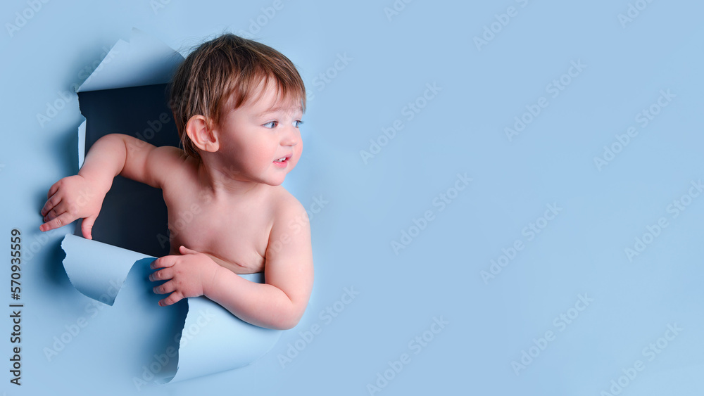 Happy baby in a hole on a paper blue background. Torn child head studio background, copy space. Kid aged one year six months Happy baby in a hole on a paper blue background. Torn child head studio background, copy space. Kid aged one year six months