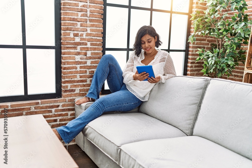Young latin woman using touchpad sitting on sofa at home Young latin woman using touchpad sitting on sofa at home