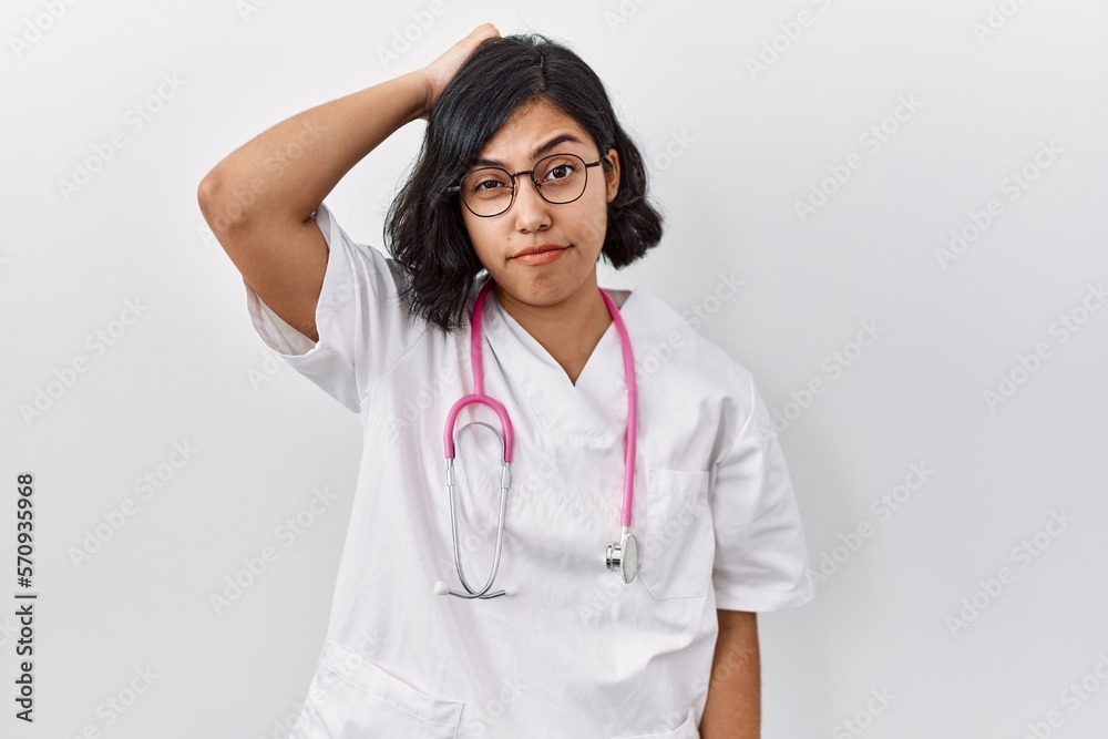 Young hispanic doctor woman wearing stethoscope over isolated background confuse and wonder about question. uncertain with doubt, thinking with hand on head. pensive concept. Young hispanic doctor woman wearing stethoscope over isolated background confuse and wonder about question. uncertain with doubt, thinking with hand on head. pensive concept.