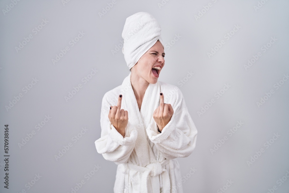 Blonde caucasian woman wearing bathrobe showing middle finger doing fuck you bad expression, provocation and rude attitude. screaming excited Blonde caucasian woman wearing bathrobe showing middle finger doing fuck you bad expression, provocation and rude attitude. screaming excited