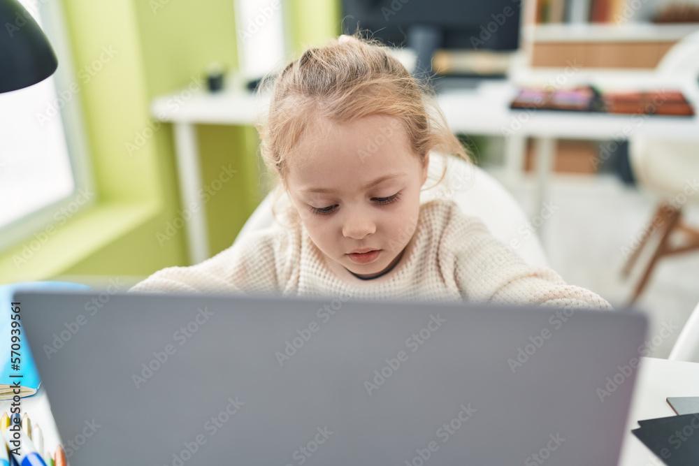 Adorable blonde girl student using laptop sitting on table at classroom Adorable blonde girl student using laptop sitting on table at classroom