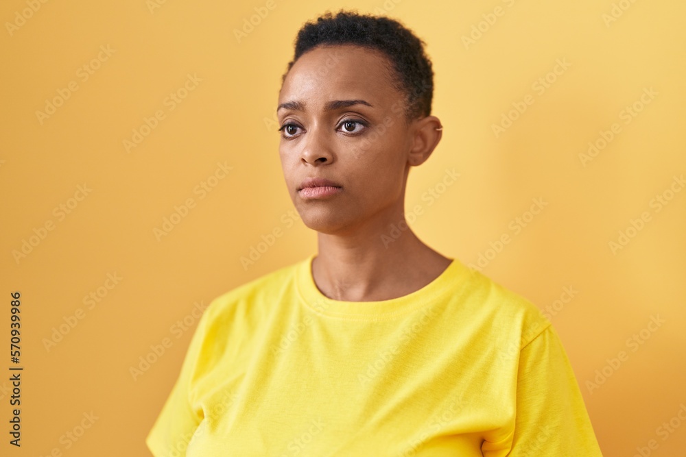 African american woman standing with serious expression over isolated yellow background African american woman standing with serious expression over isolated yellow background