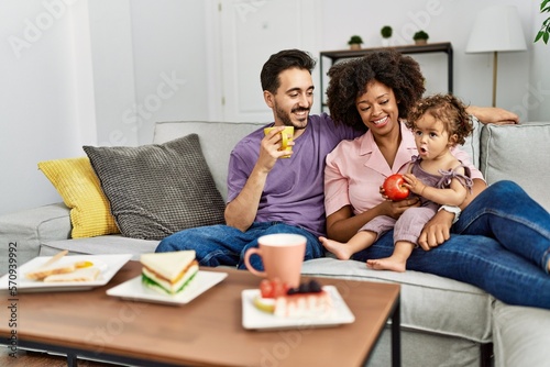 Couple and daughter having breakfast sitting on sofa at home