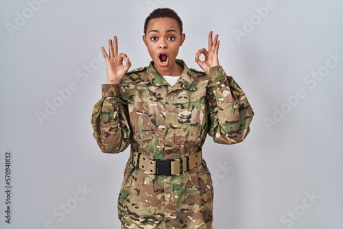 Beautiful african american woman wearing camouflage army uniform looking surprised and shocked doing ok approval symbol with fingers. crazy expression