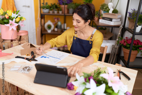 Middle age hispanic woman florist using touchpad writing on document at flower shop