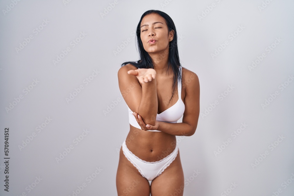 Fototapeta premium Hispanic woman wearing lingerie looking at the camera blowing a kiss with hand on air being lovely and sexy. love expression.