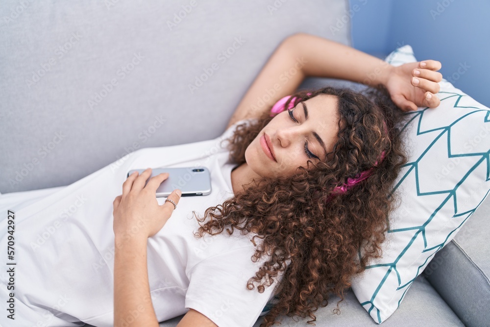 Naklejka premium Young beautiful hispanic woman listening to music sleeping on sofa at home