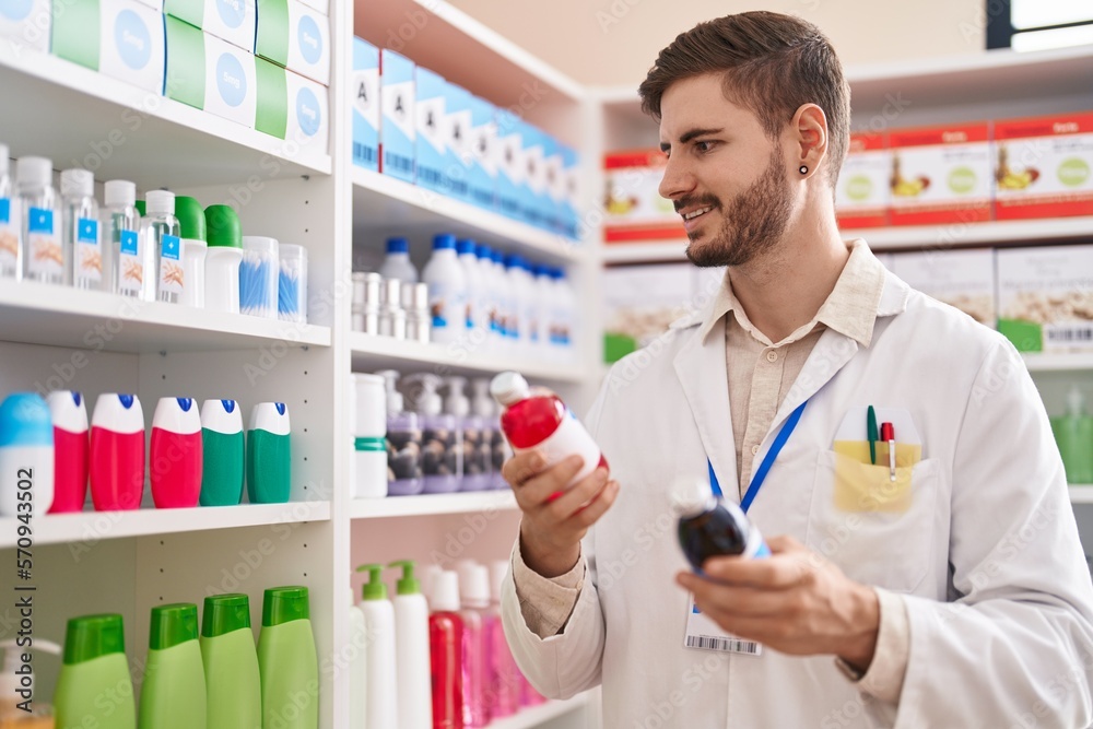 Young caucasian man pharmacist smiling confident holding medication bottles at pharmacy