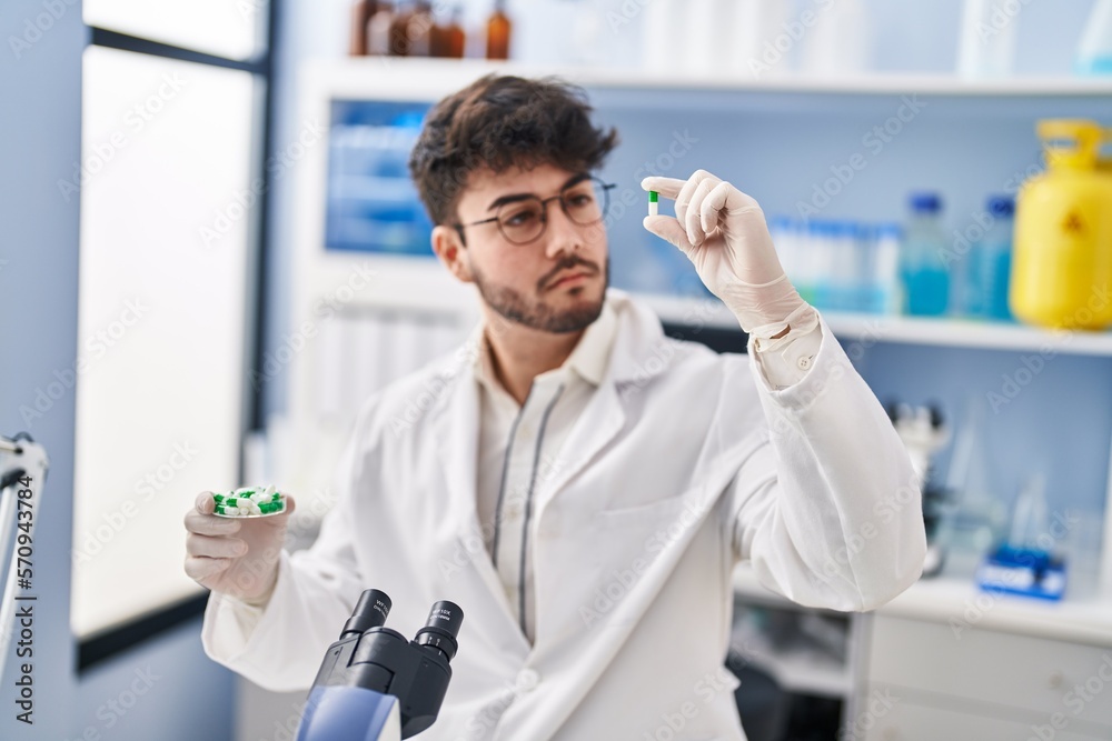 Young hispanic man scientist holding pills at laboratory Young hispanic man scientist holding pills at laboratory