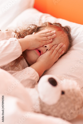 Adorable blonde toddler stressed lying on bed covering eyes with hands at bedroom