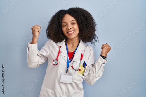 Young african american woman wearing doctor uniform and stethoscope celebrating surprised and amazed for success with arms raised and eyes closed. winner concept.