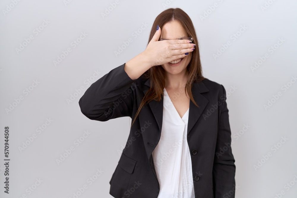 Beautiful brunette woman wearing business jacket and glasses smiling and laughing with hand on face covering eyes for surprise. blind concept. Beautiful brunette woman wearing business jacket and glasses smiling and laughing with hand on face covering eyes for surprise. blind concept.