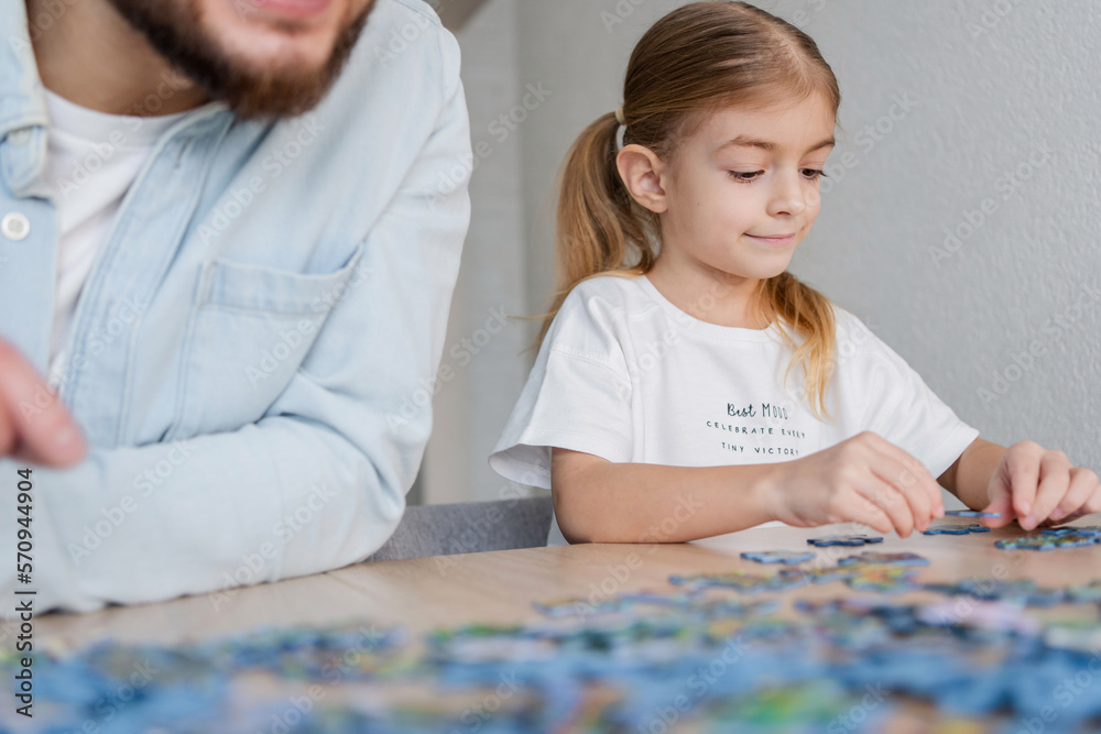 Father and daughter having fun sitting at table at home doing jigsaw puzzle together. Father and daughter having fun sitting at table at home doing jigsaw puzzle together.