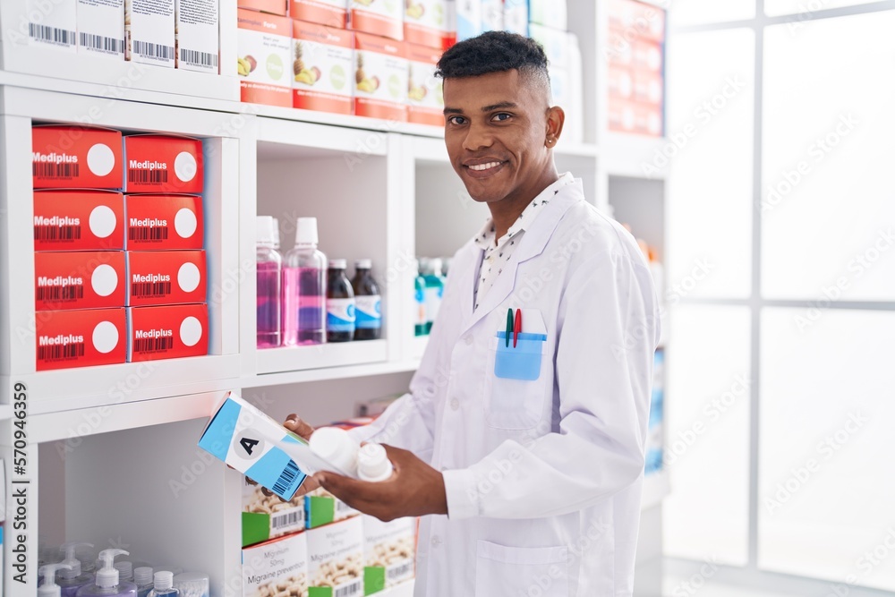 Young latin man pharmacist holding pills bottle reading prescription at pharmacy