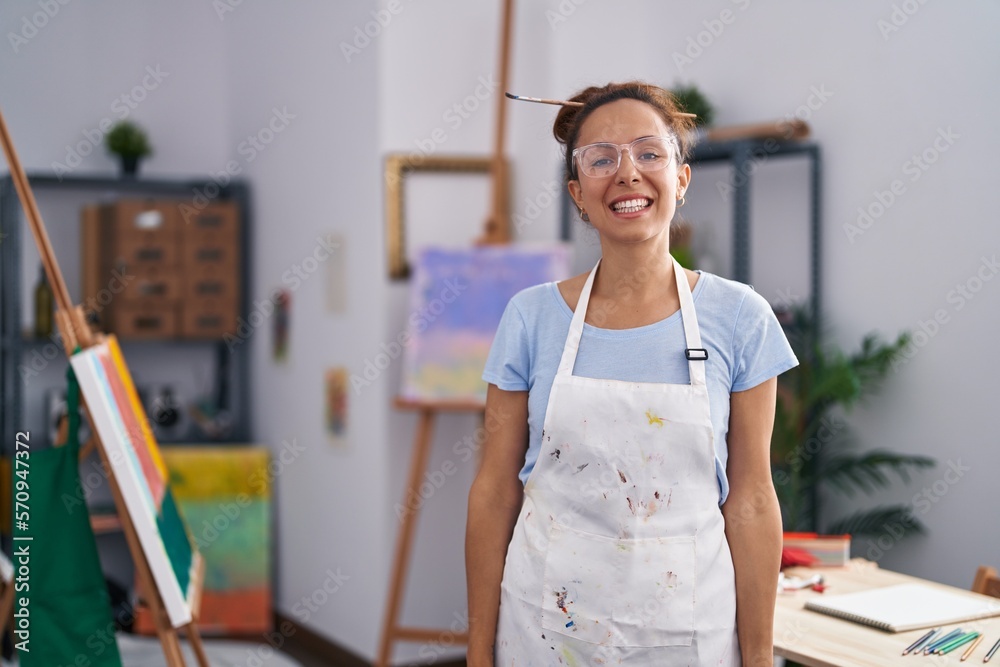 Brunette woman painting at art studio looking positive and happy standing and smiling with a confident smile showing teeth Brunette woman painting at art studio looking positive and happy standing and smiling with a confident smile showing teeth
