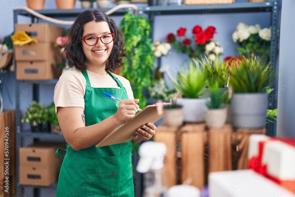 Young woman florist smiling confident writing on clipboard at florist