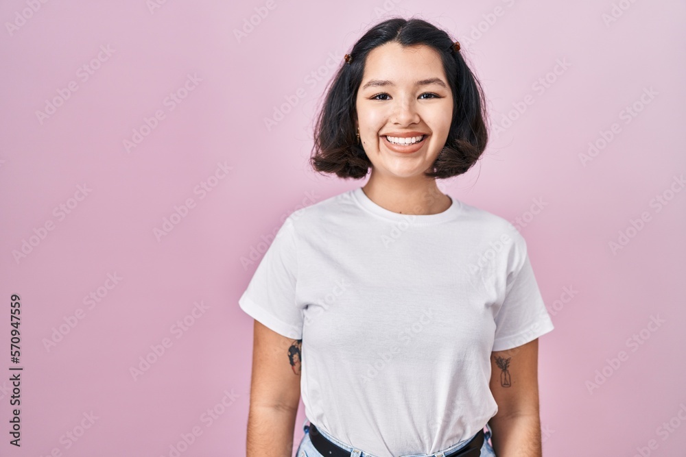 Fototapeta premium Young hispanic woman wearing casual white t shirt over pink background with a happy and cool smile on face. lucky person.