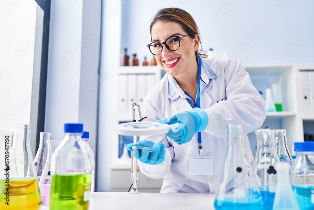 Young beautiful hispanic woman scientist smiling confident using magnifying glass at laboratory Young beautiful hispanic woman scientist smiling confident using magnifying glass at laboratory