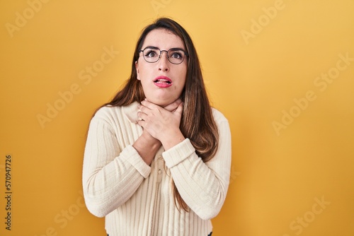 Young hispanic woman standing over yellow background shouting and suffocate because painful strangle. health problem. asphyxiate and suicide concept.