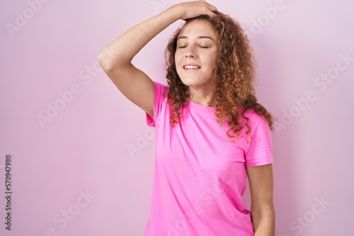 Young caucasian woman standing over pink background smiling confident touching hair with hand up gesture, posing attractive and fashionable