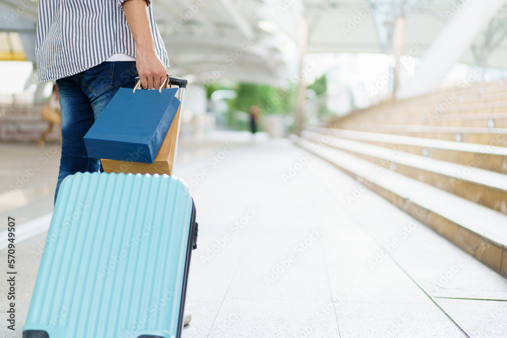 Asian young man dragging a suitcase along the city or airport terminal with shopping bags. Man traveling in the city or urban area. Asian young man dragging a suitcase along the city or airport terminal with shopping bags. Man traveling in the city or urban area.