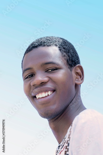 Portrait of a laughing young man wearing a traditionnal white shirt, 19 years old, outdoors, sunny day, blue sky, photo