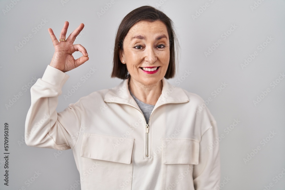 Middle age hispanic woman standing over isolated background smiling positive doing ok sign with hand and fingers. successful expression. Middle age hispanic woman standing over isolated background smiling positive doing ok sign with hand and fingers. successful expression.