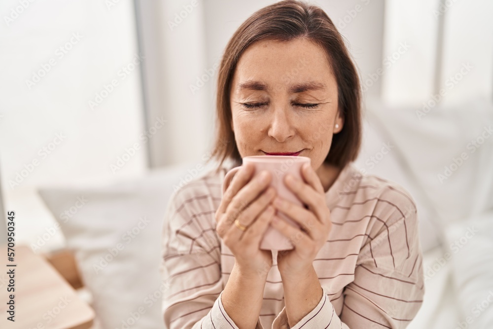 Middle age woman smelling coffee sitting on bed at bedroom Middle age woman smelling coffee sitting on bed at bedroom