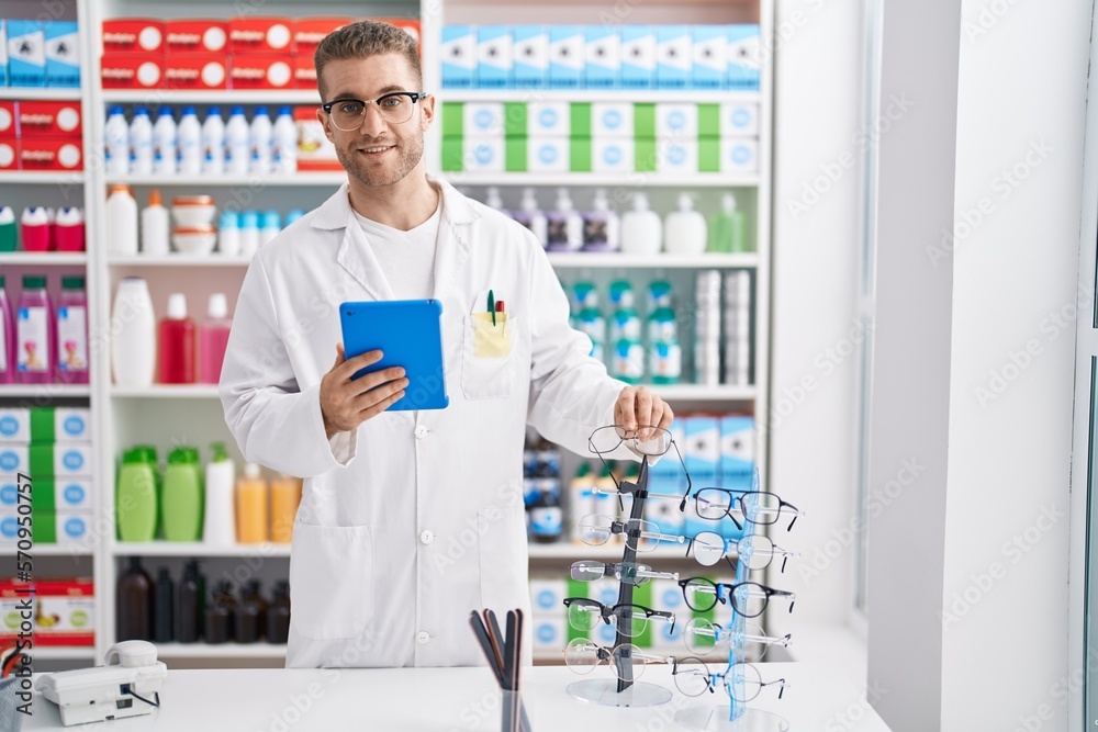 Young caucasian man pharmacist using touchpad holding glasses at pharmacy