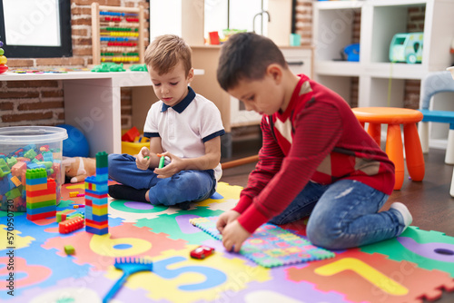 Two kids playing with construction blocks and maths puzzle game sitting on floor at kindergarten