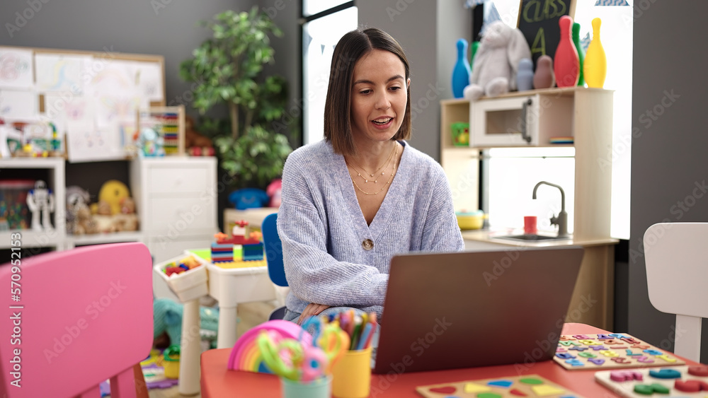 Young beautiful hispanic woman working as a teacher using laptop at kindergarten Young beautiful hispanic woman working as a teacher using laptop at kindergarten