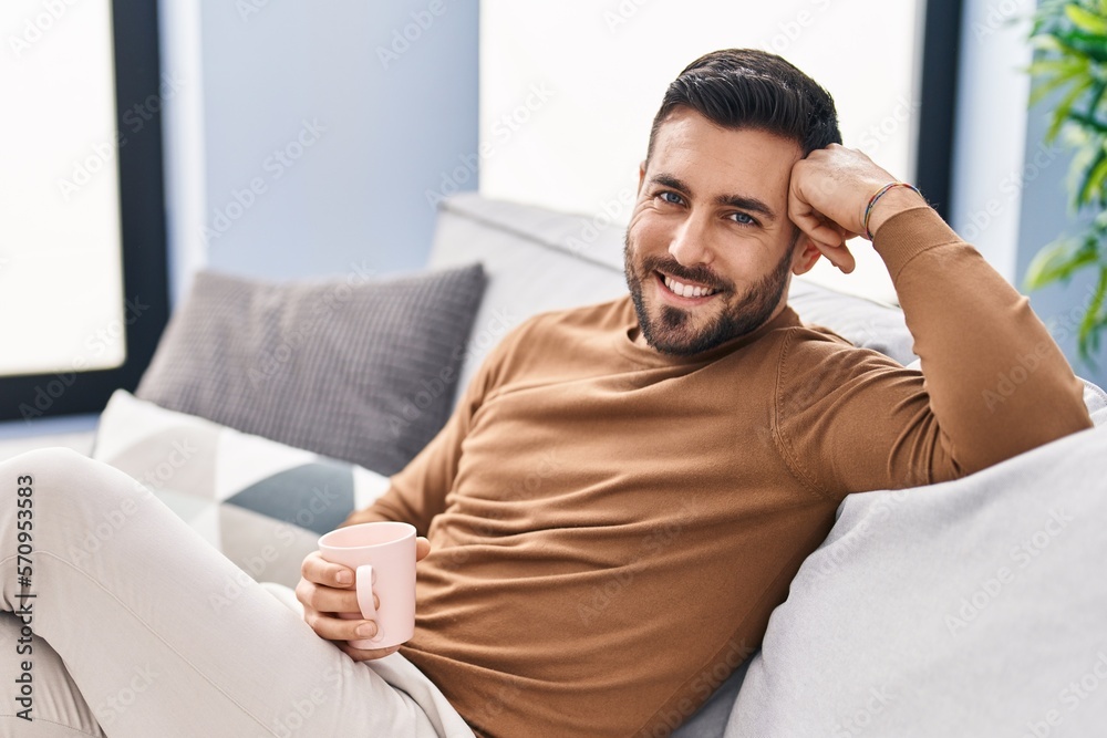 Young hispanic man drinking coffee sitting on sofa at home Young hispanic man drinking coffee sitting on sofa at home