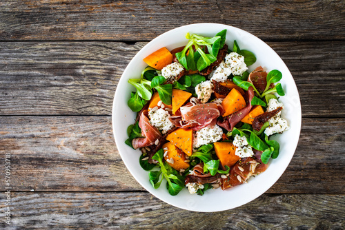 Tasty salad - prosciutto crudo, sweet potatoes, smoked white cheese and fresh vegetables on wooden table 