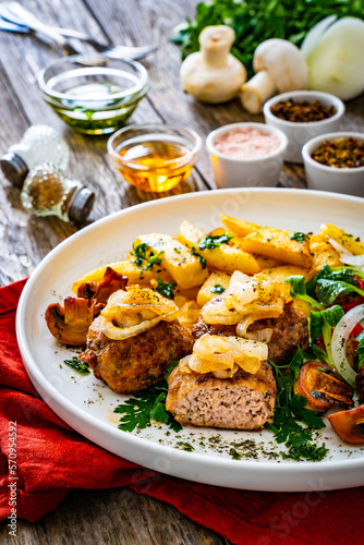 Fried pork meatballs with fried onion, french fries and fresh vegetables on wooden table
