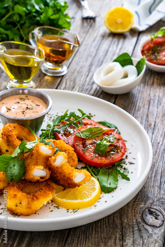 Fried breaded calamari rings with lemon and fresh vegetables on wooden table
Fried breaded calamari rings with lemon and fresh vegetables on wooden table