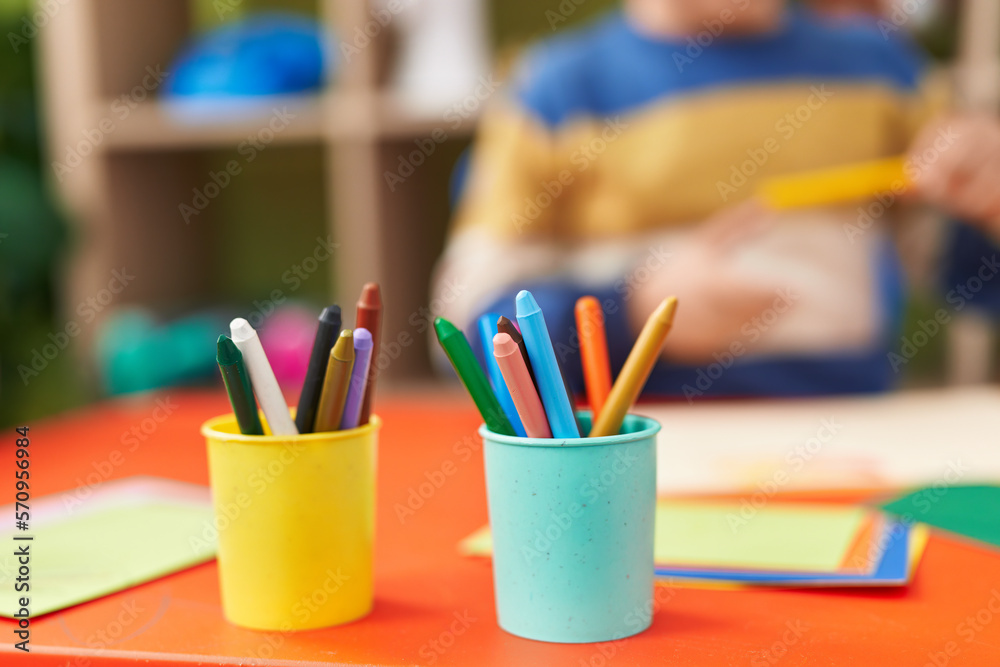 Adorable hispanic boy preschool student sitting on table holding pencil at kindergarten Adorable hispanic boy preschool student sitting on table holding pencil at kindergarten