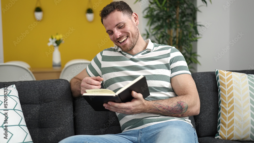 Young caucasian man reading a book sitting on the sofa at home