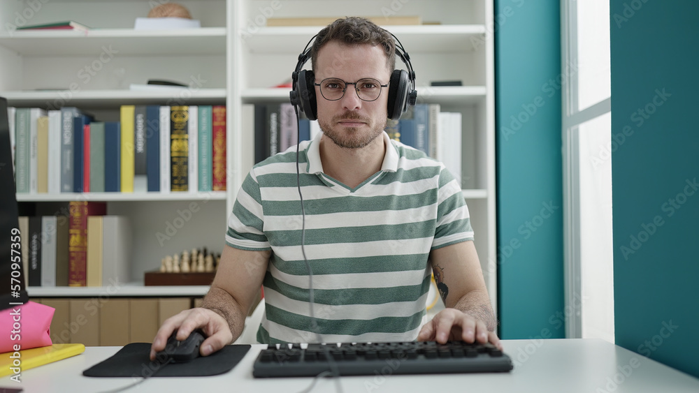 Fototapeta premium Young caucasian man using computer wearing headphones at library university