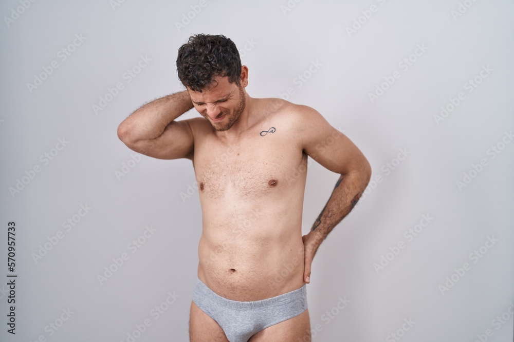 Young hispanic man standing shirtless wearing underware suffering of neck ache injury, touching neck with hand, muscular pain