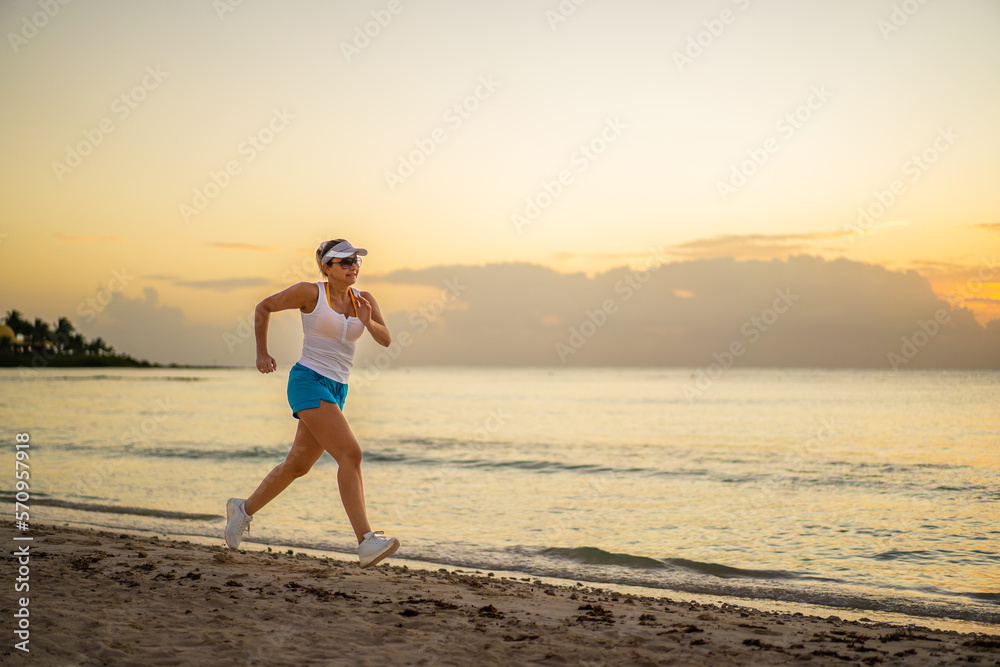 Woman running, walking on sunny, tropical beach at daybreak

