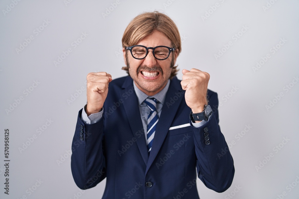 Caucasian man with mustache wearing business clothes excited for success with arms raised and eyes closed celebrating victory smiling. winner concept. Caucasian man with mustache wearing business clothes excited for success with arms raised and eyes closed celebrating victory smiling. winner concept.