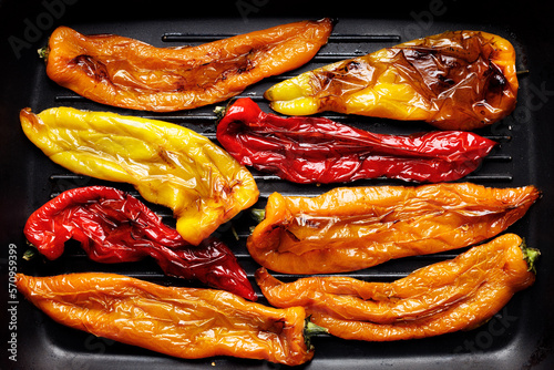 Grilled peppers of different colors cut in half on a grill plate, top view photo