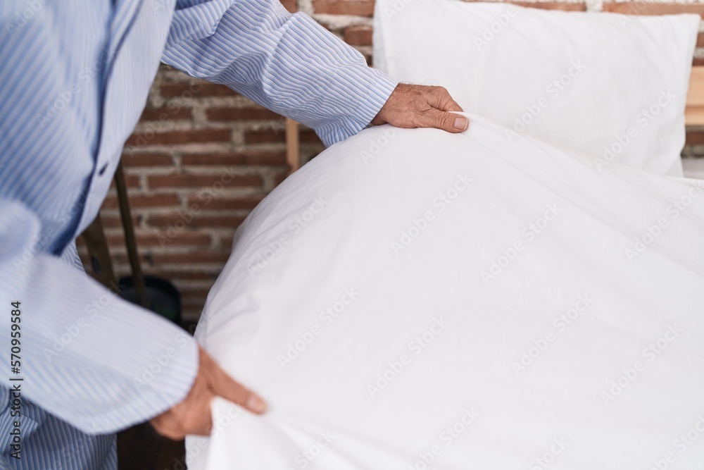 Middle age grey-haired man make bed at bedroom Middle age grey-haired man make bed at bedroom