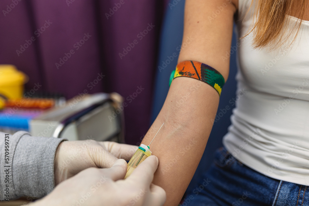 Preparation for blood test with pretty young woman by female doctor medical uniform on the table in white bright room. Nurse pierces the patient's arm vein with needle blank tube