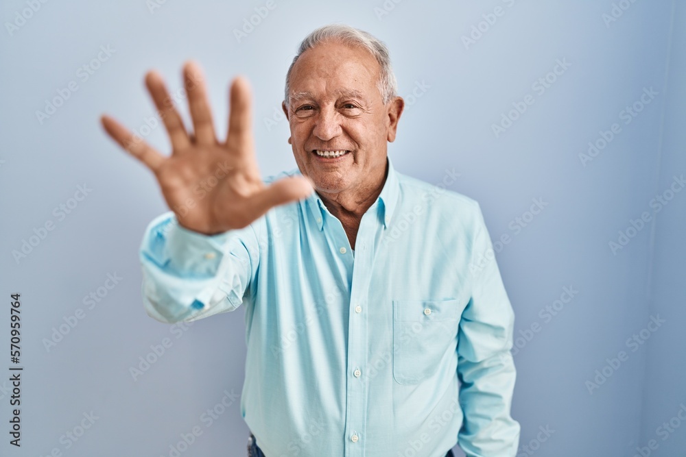 Senior man with grey hair standing over blue background showing and pointing up with fingers number five while smiling confident and happy. Senior man with grey hair standing over blue background showing and pointing up with fingers number five while smiling confident and happy.