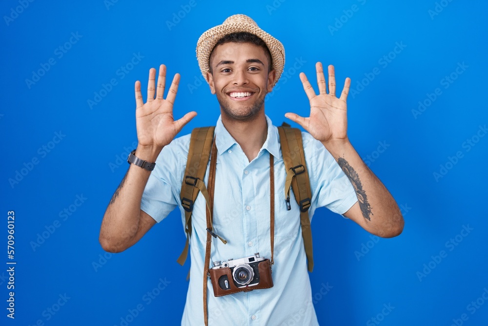 Naklejka premium Brazilian young man holding vintage camera showing and pointing up with fingers number ten while smiling confident and happy.